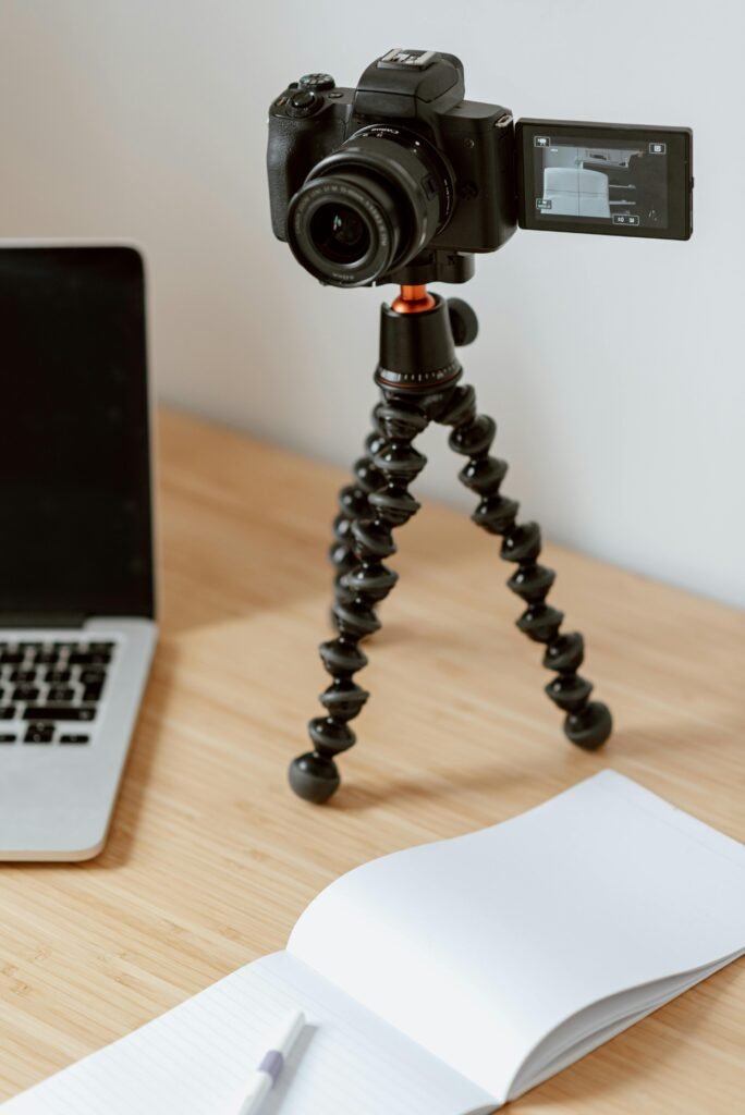 A creative workspace featuring a camera on a tripod, laptop, and open notebook.